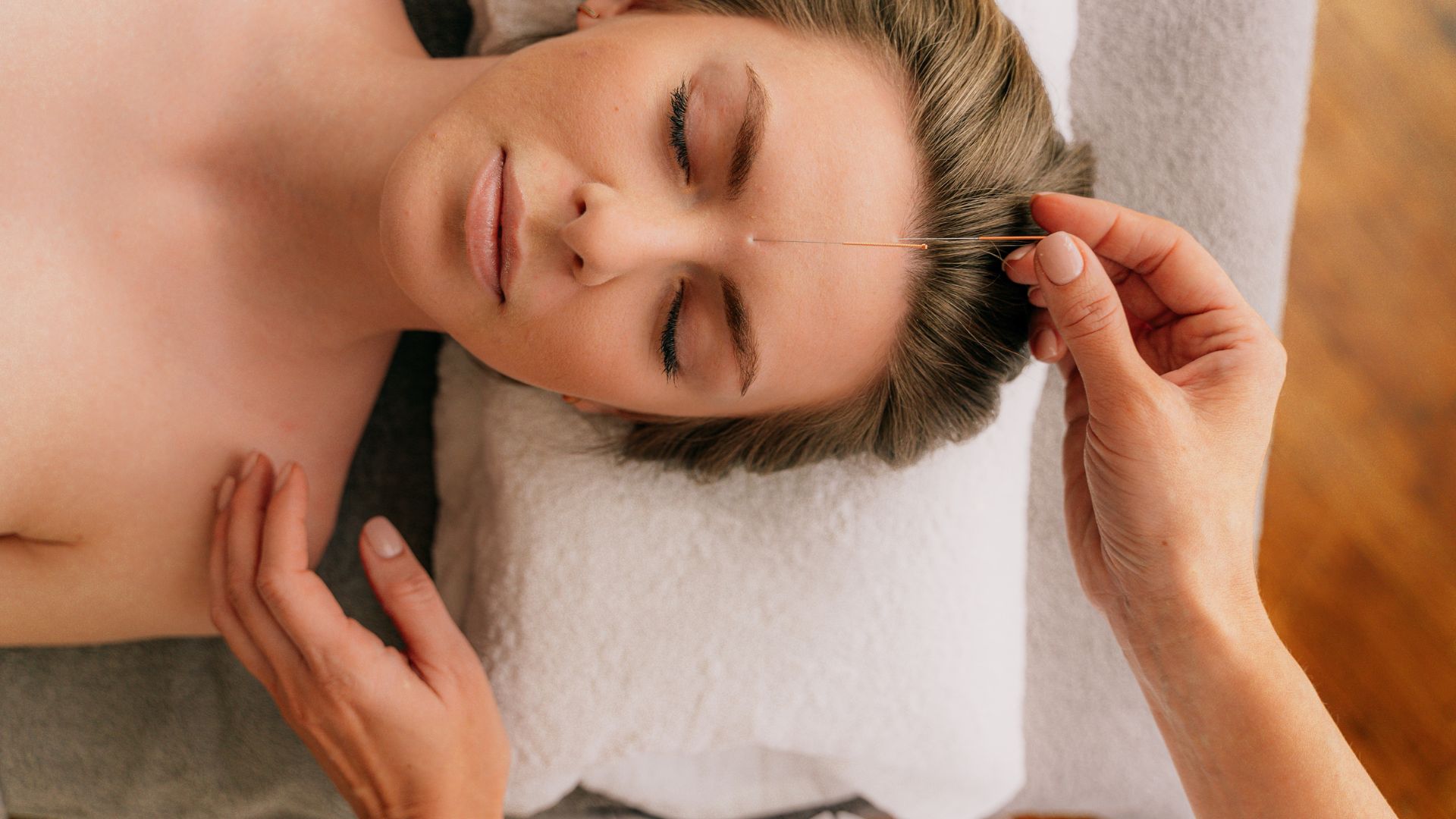 Person receiving facial treatment with acupuncture needle, eyes closed