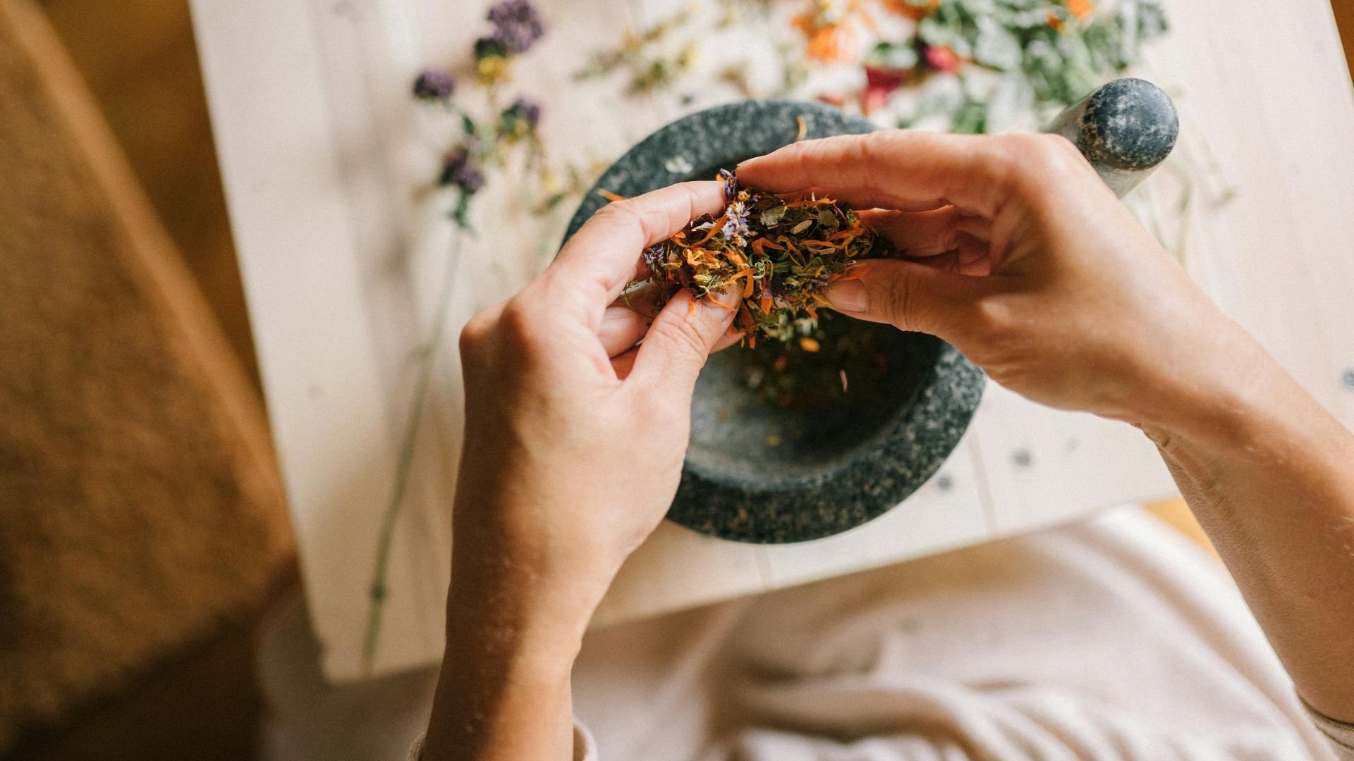 Hands grinding dried herbs and flowers in a stone mortar